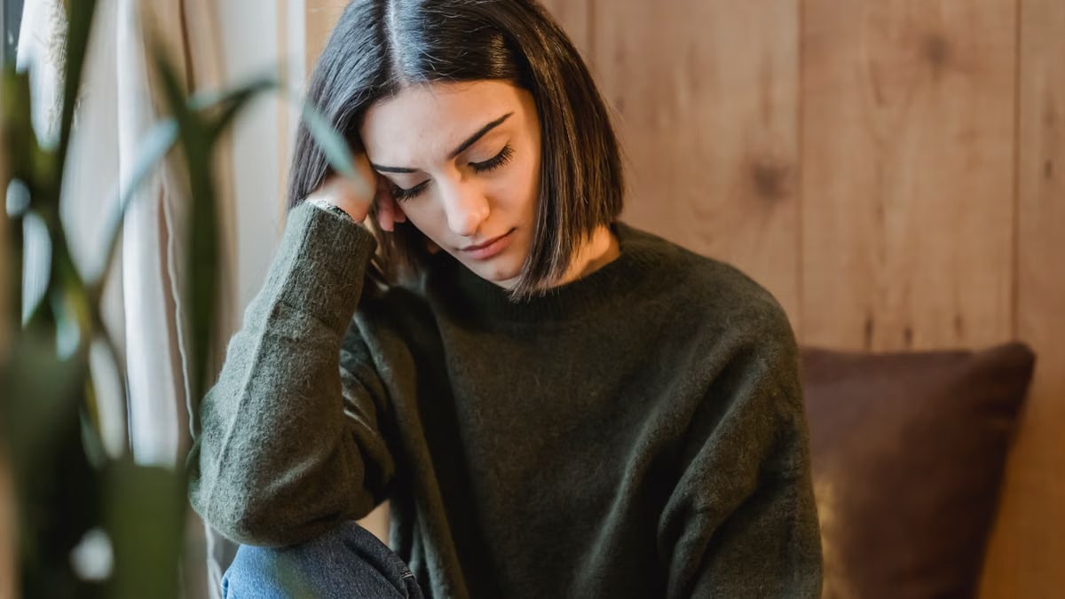 Tired female with closed eyes leaning on hand while having break and nap near window